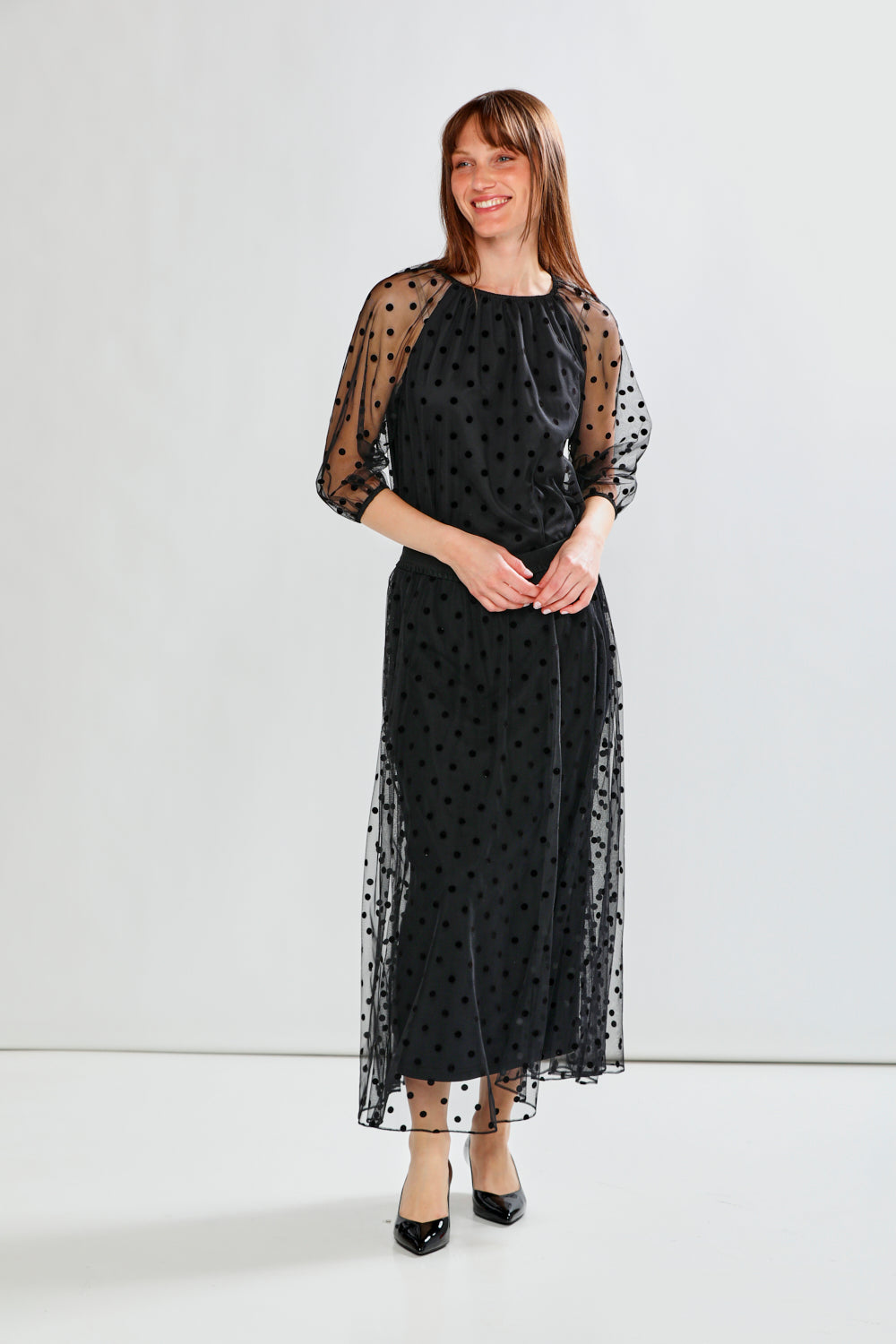 Person wearing a black polka dot tulle skirt with a plain background