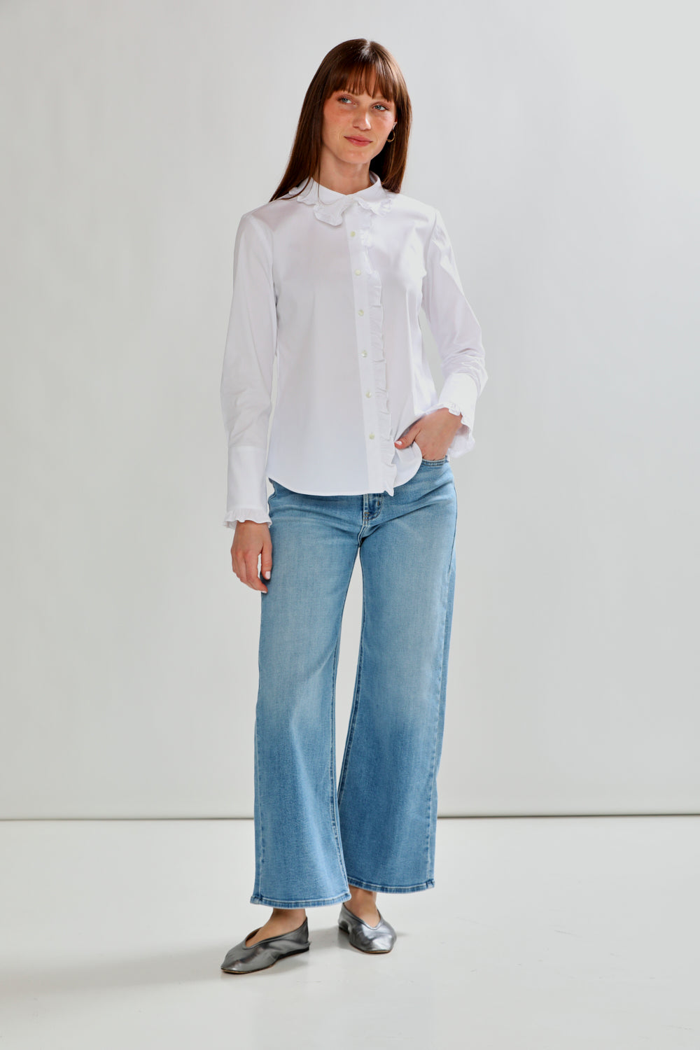 Woman wearing a white blouse and light blue jeans against a plain background