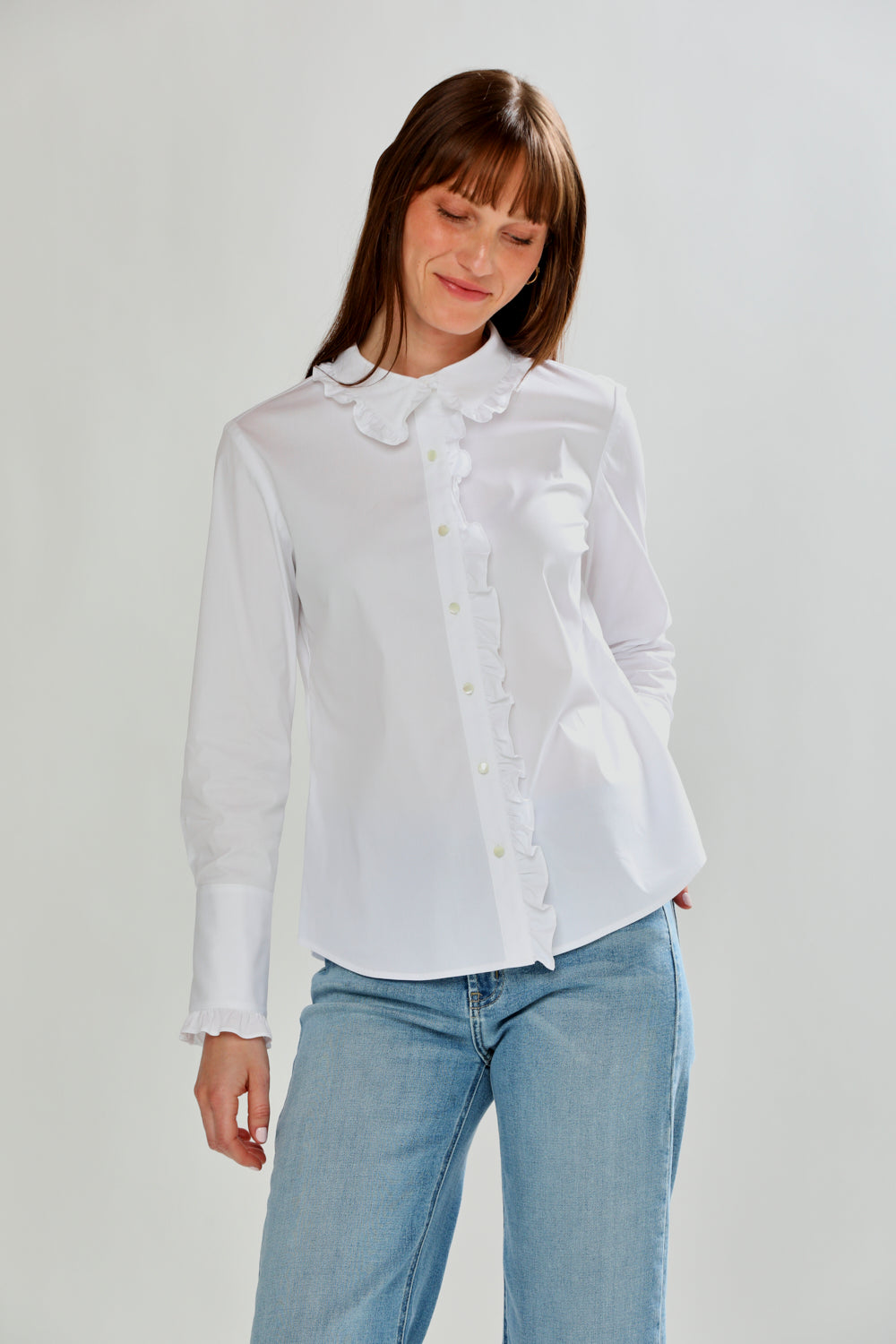 Woman wearing a white blouse with ruffled details and light blue jeans on a plain background