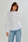 Woman wearing a white blouse with ruffled details and light blue jeans on a plain background