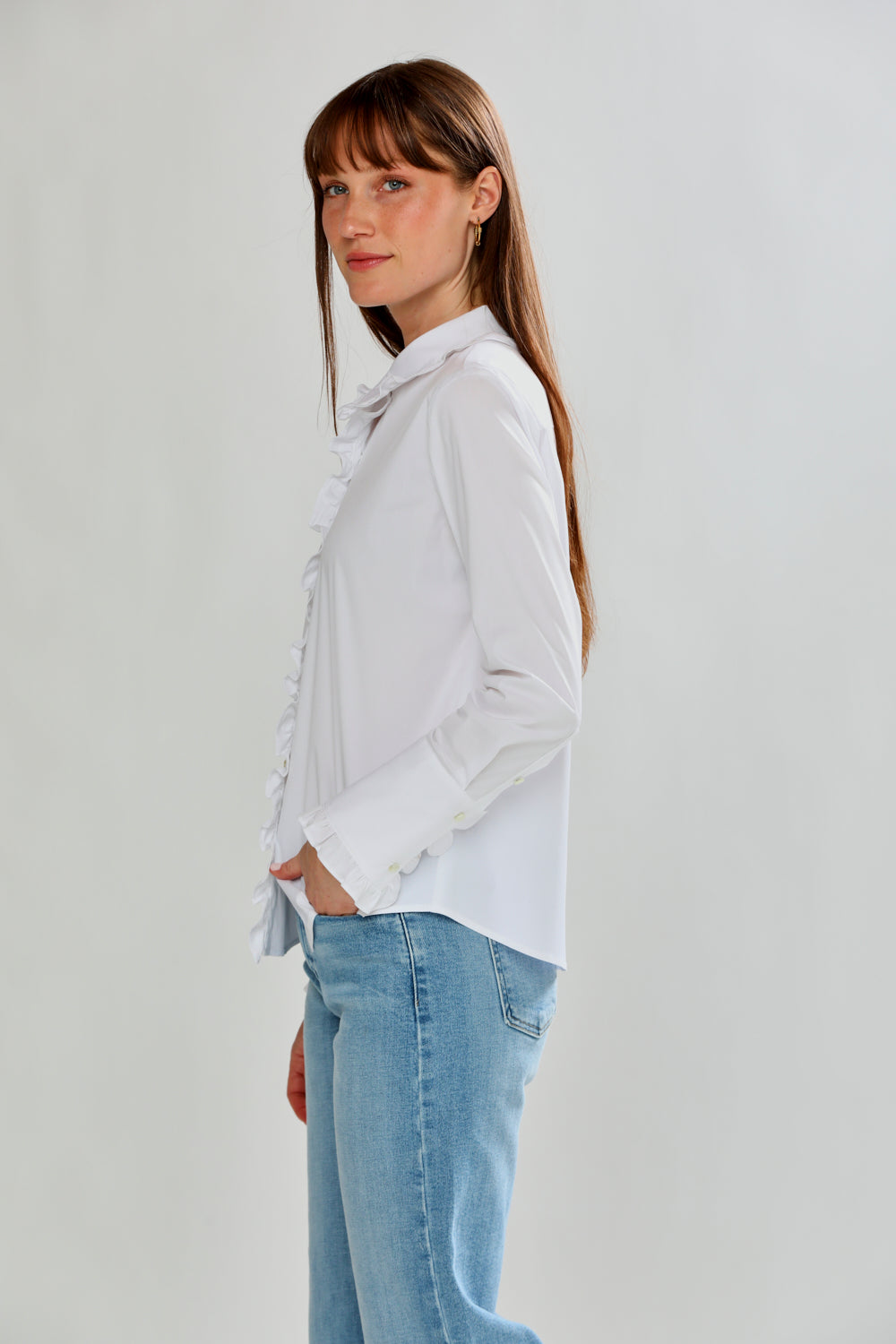 Woman wearing a white blouse and light blue jeans against a plain background