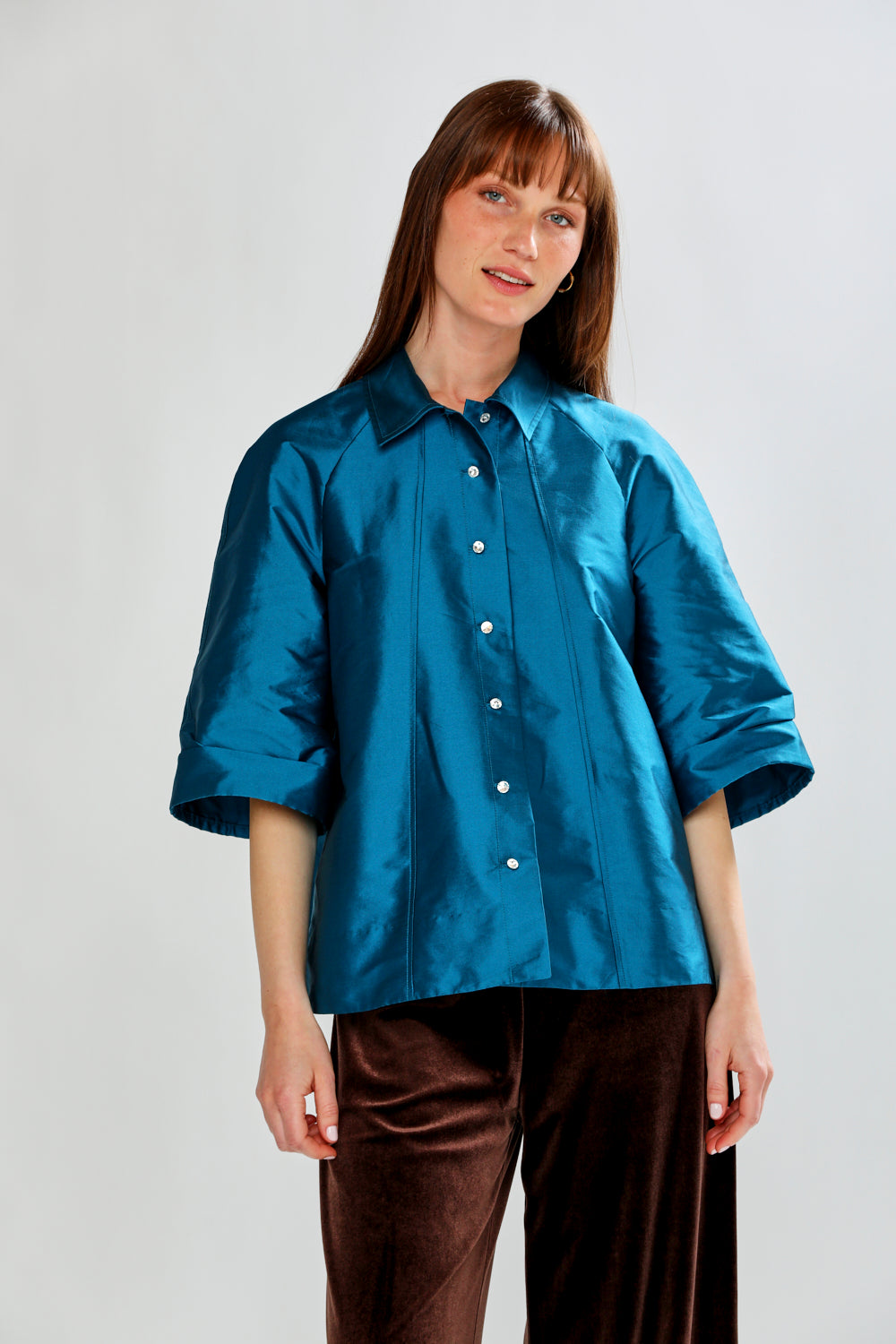 Woman wearing a blue satin shirt and brown pants on a plain background