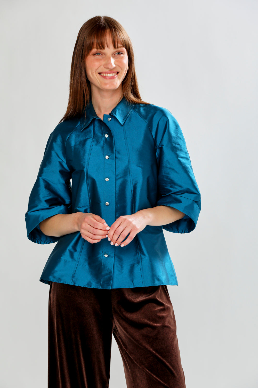 Woman wearing a blue shirt and brown pants against a white background