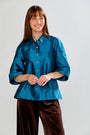 Woman wearing a blue shirt and brown pants against a white background