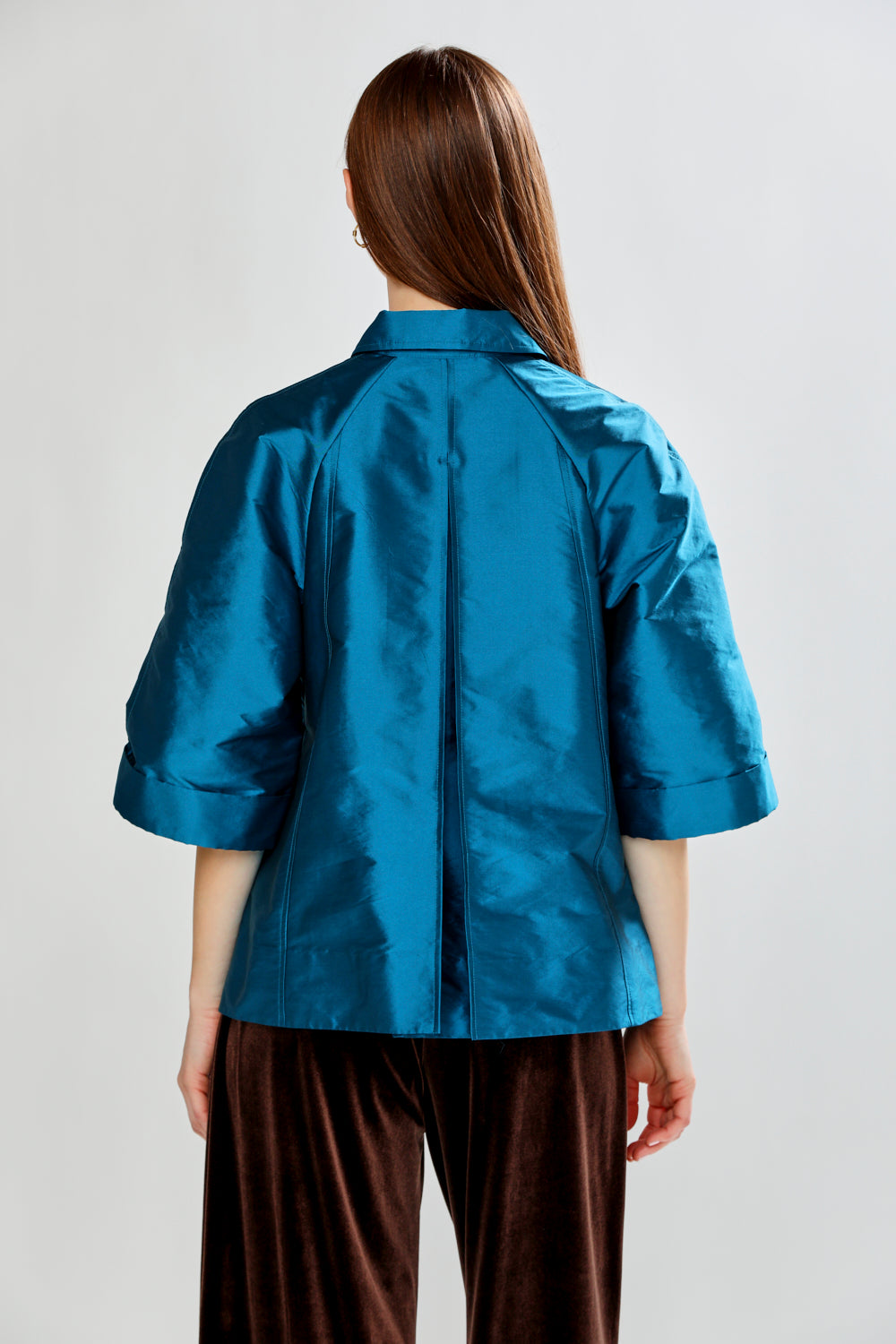 Person wearing a blue satin shirt and brown pants on a plain background