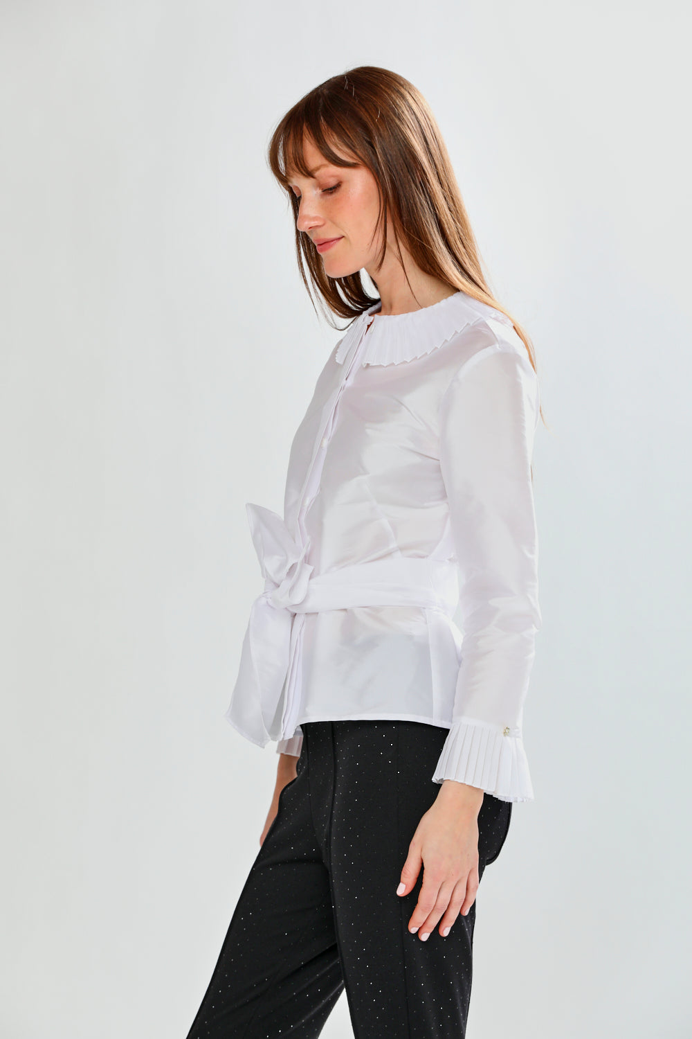 Woman wearing a white blouse with a tie detail on a light gray background