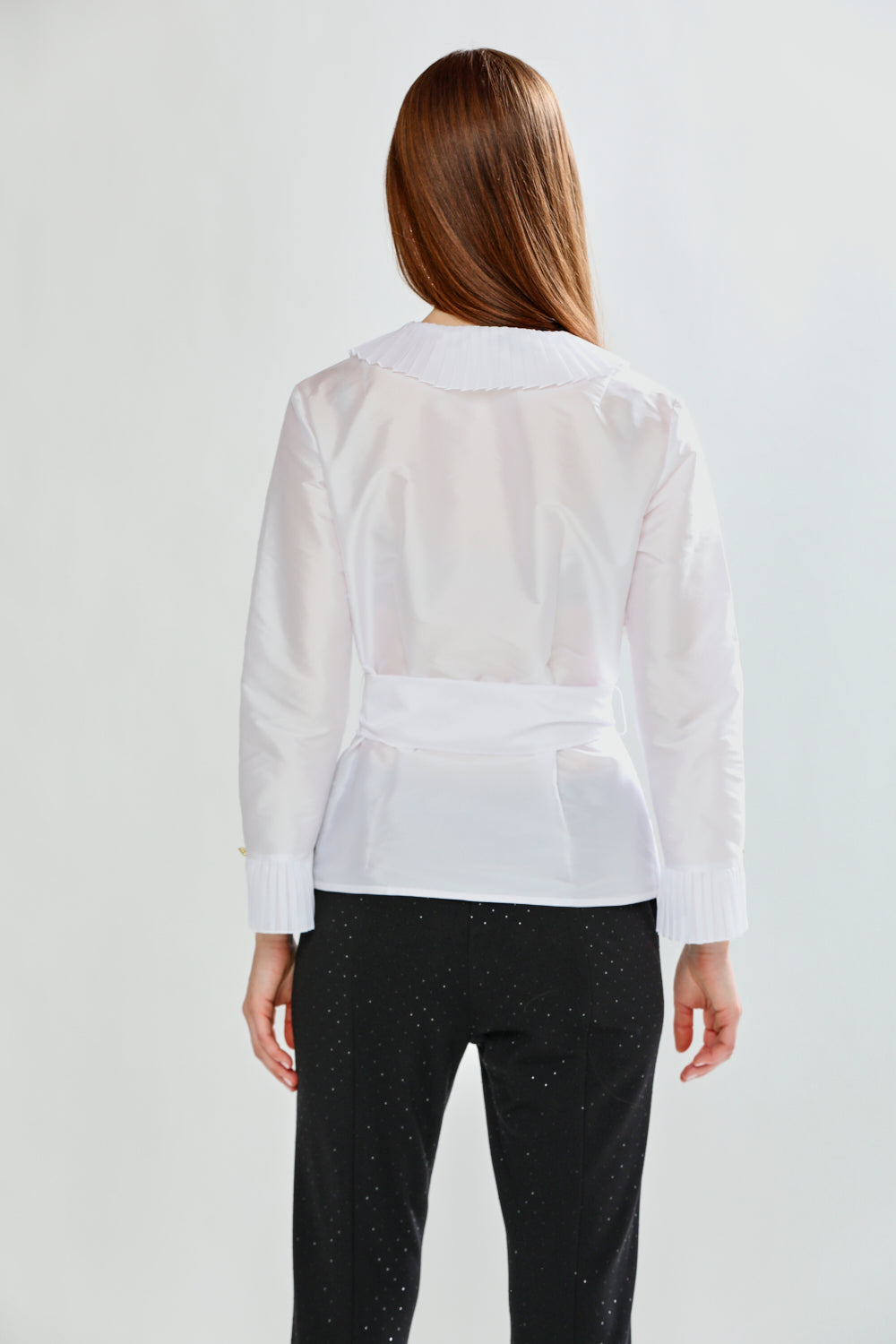 Person wearing a white blouse and black pants on a plain background