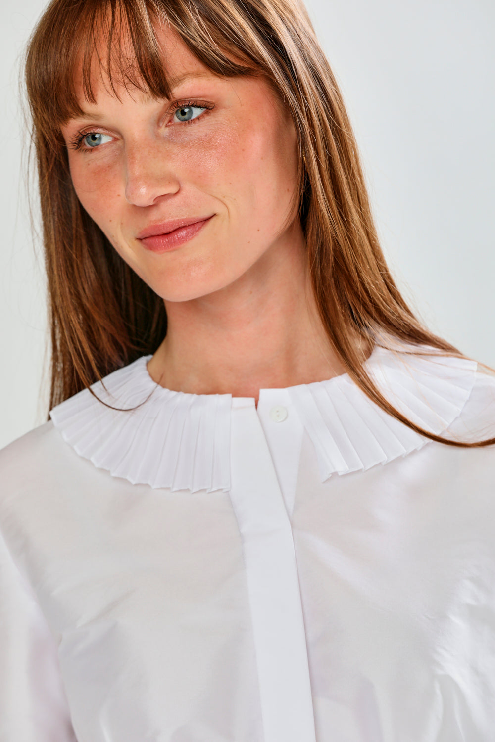 Woman wearing a white blouse with a ruffled collar against a plain background