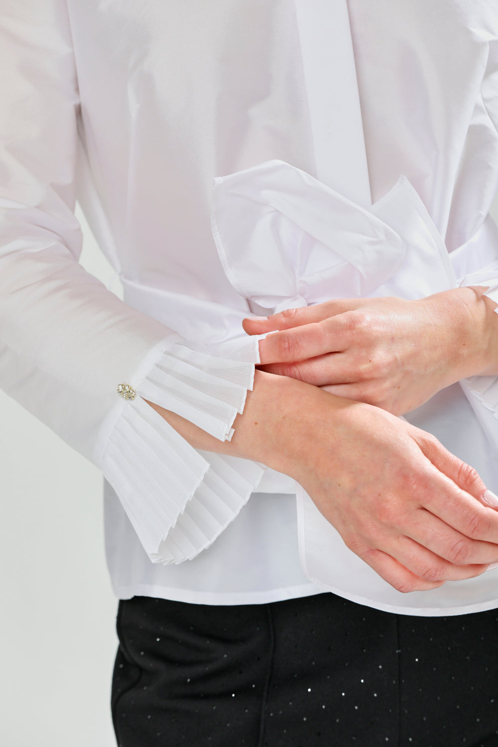 Close-up of a person wearing a white blouse with ruffled cuffs on a light background