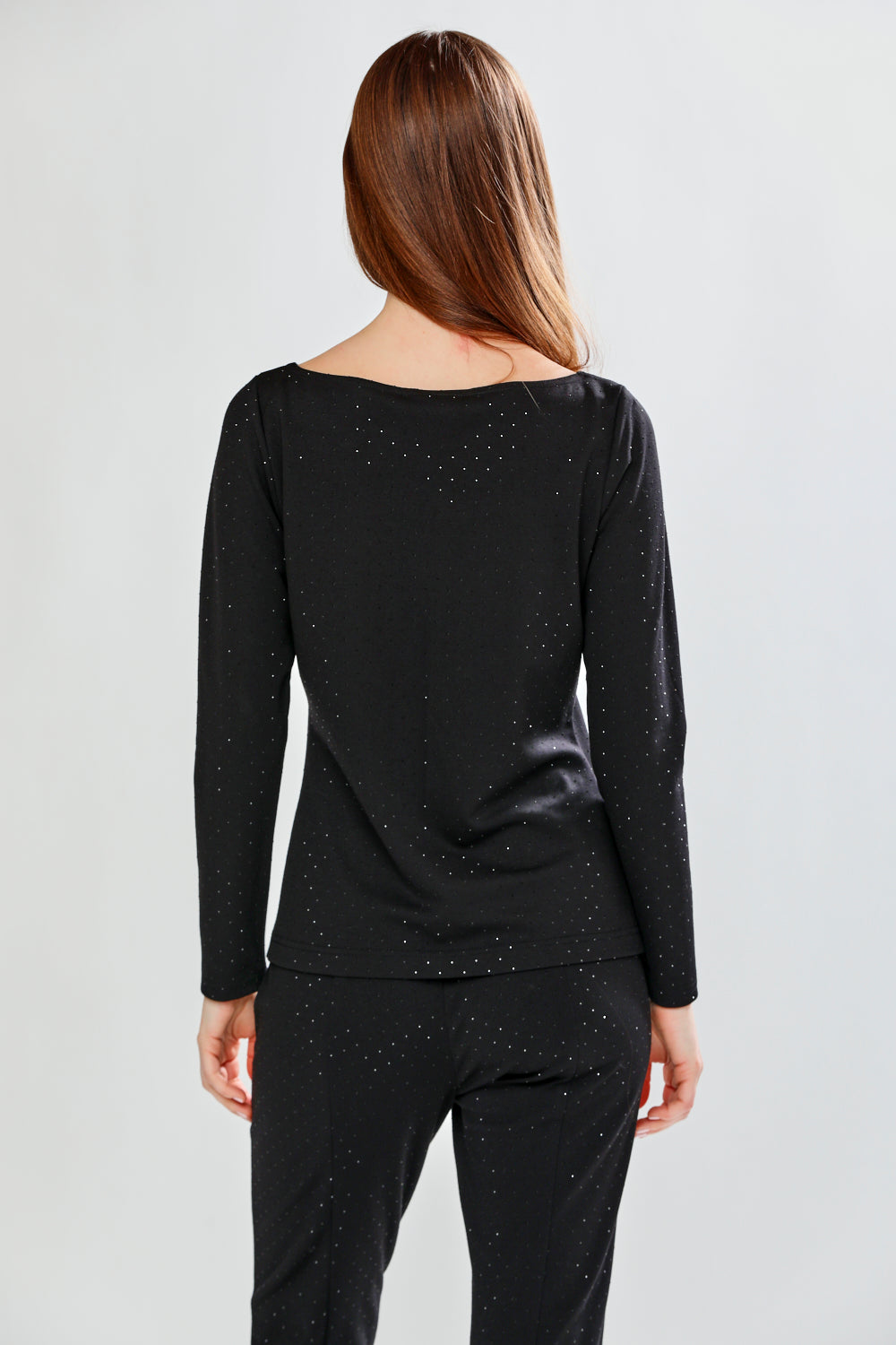 Person wearing a black long-sleeve top with subtle pattern on a plain background