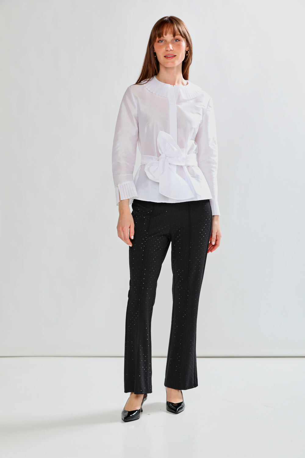 Woman wearing a white blouse with a bow and black pants on a white background
