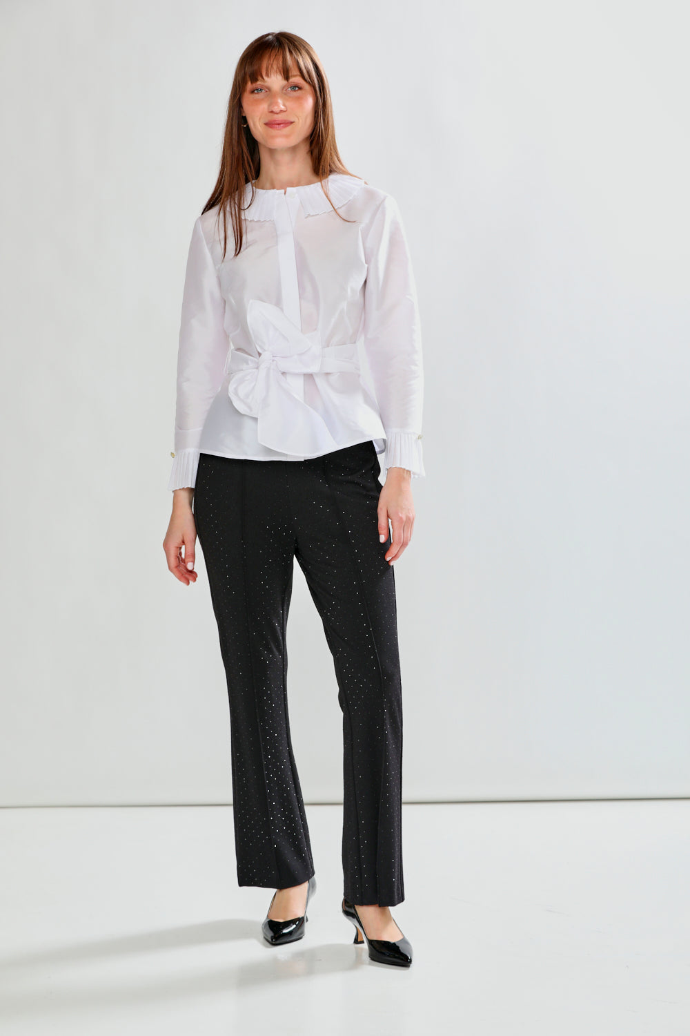 Woman wearing a white blouse with a bow and black pants on a white background