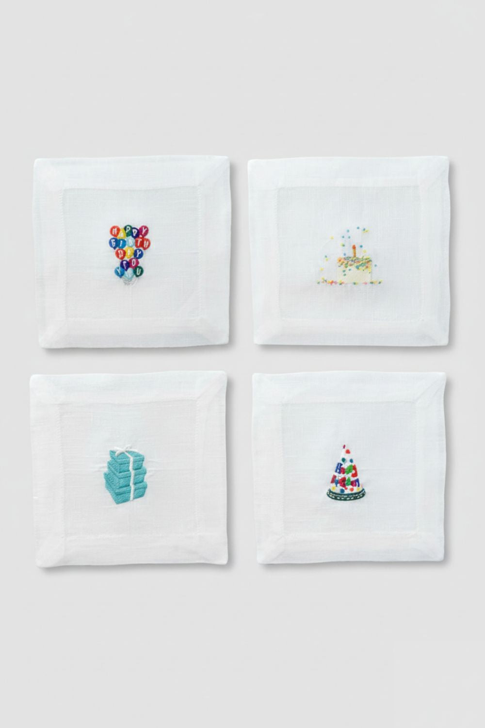 Four white napkins with embroidered designs on a light gray background