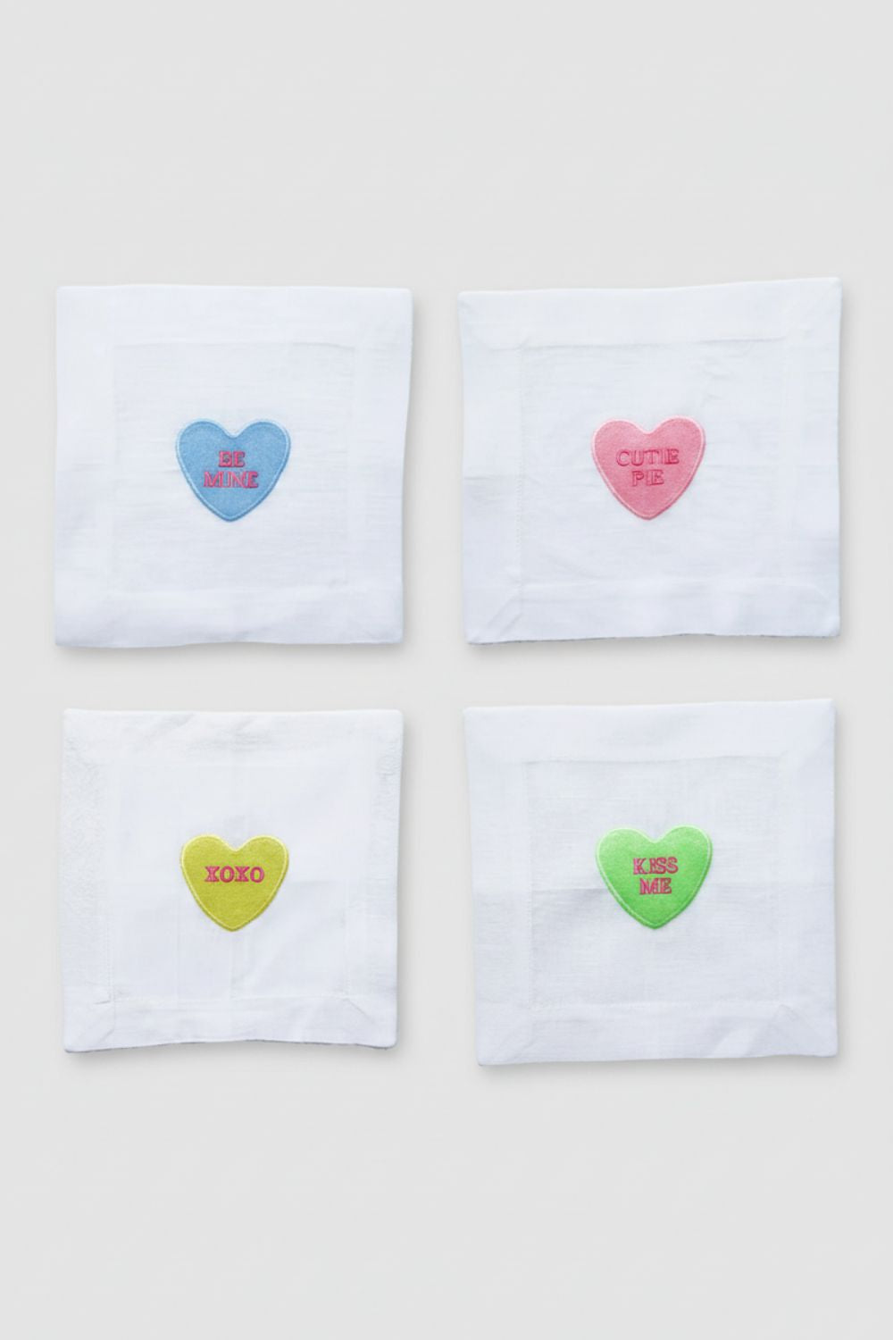 Four white napkins with colorful heart-shaped candies on a light beige background
