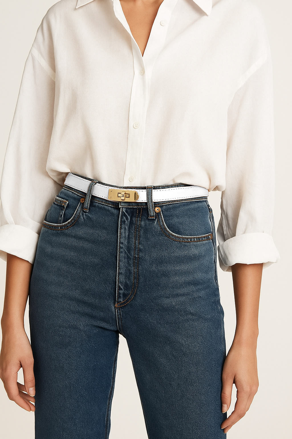 Person wearing a white shirt and blue jeans with a gold belt on a plain background