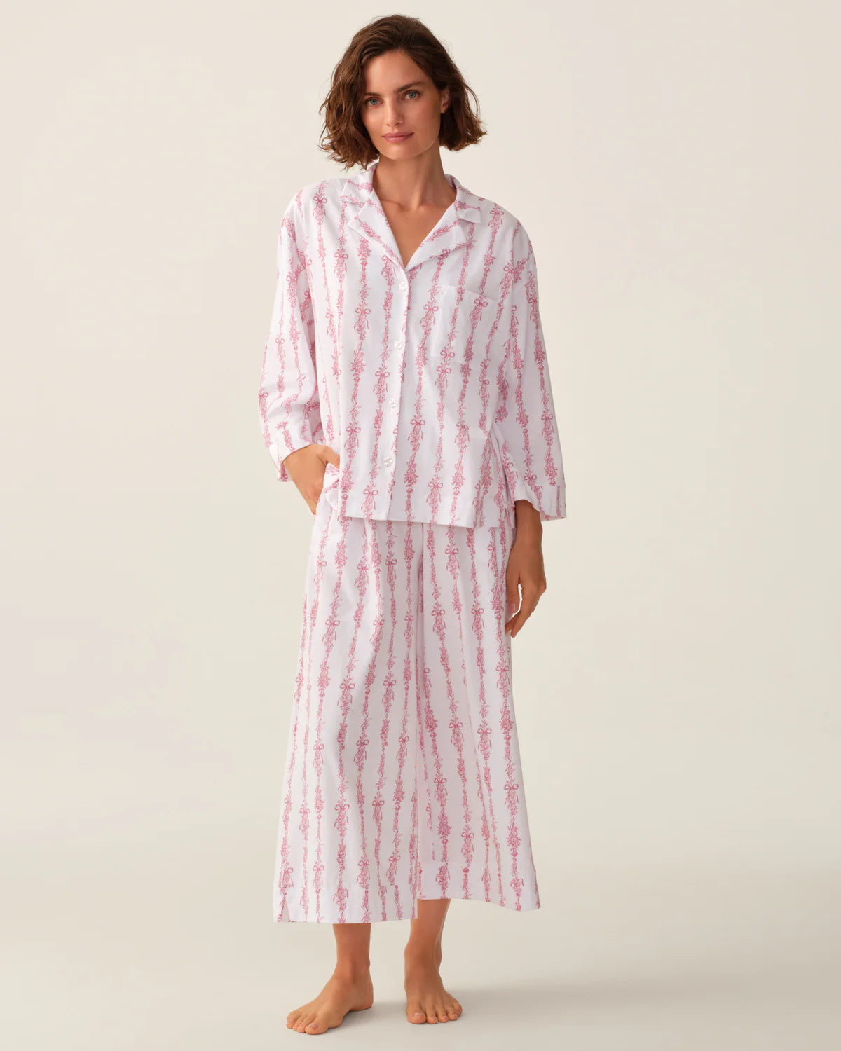 A woman modeling a matching two-piece pajama set with a white base and pink vertical tie-dye style stripes, photographed against a plain light beige studio background.