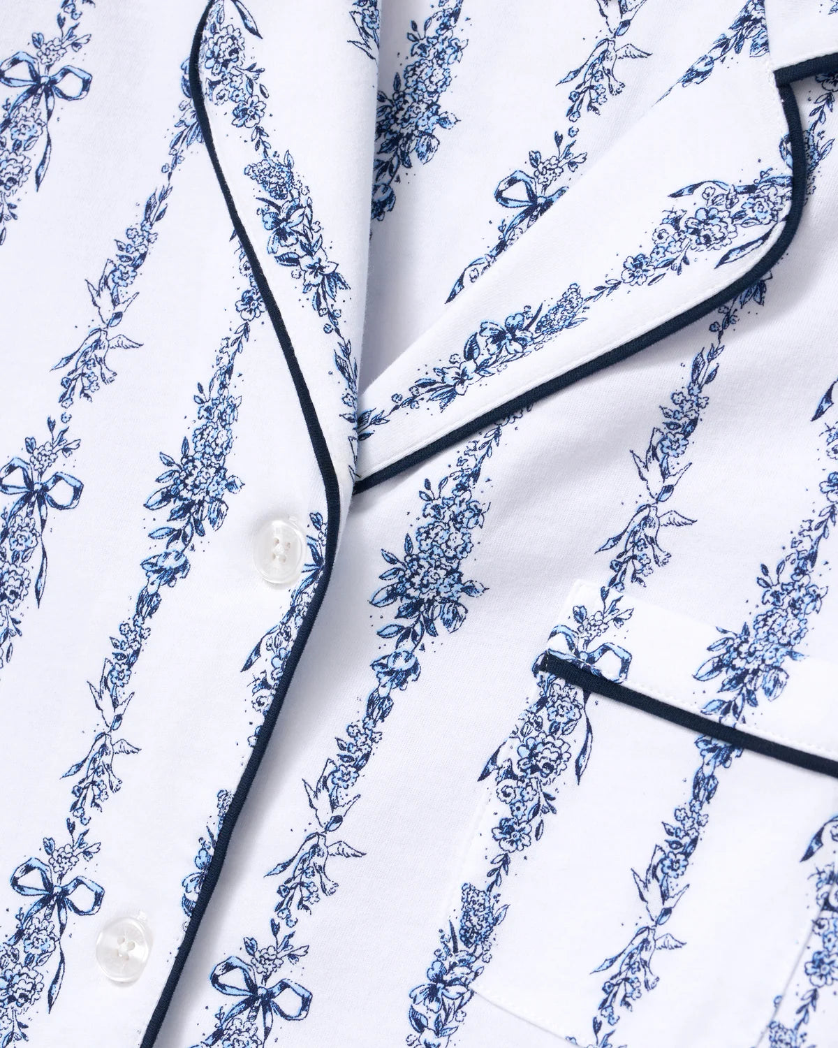 Close-up of a white pajama shirt with a blue floral toile pattern and navy piping trim.