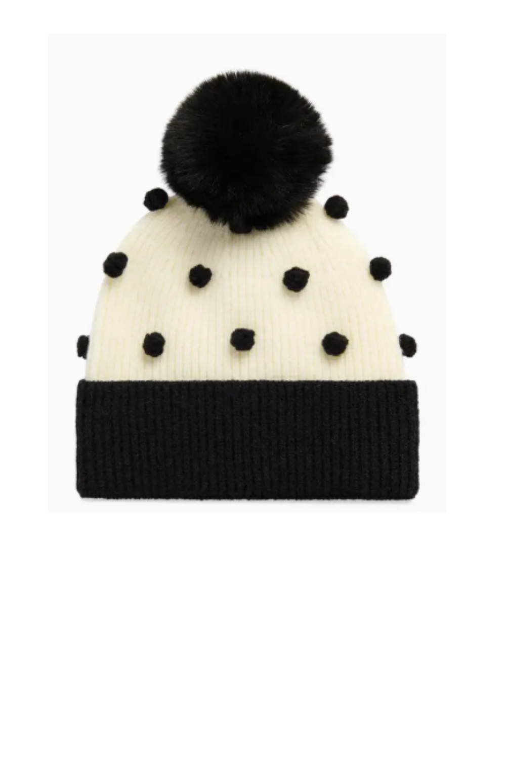 A cream knit beanie hat with black pom-poms and a black ribbed cuff, topped with a large black faux-fur pom-pom, shown against a plain white background.