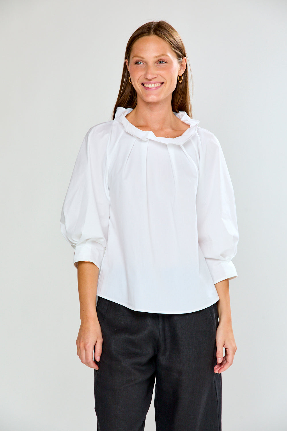 Woman wearing a white blouse and black pants against a plain background