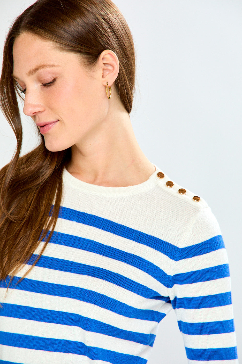 Woman wearing a blue and white striped sweater with gold buttons on a light gray background