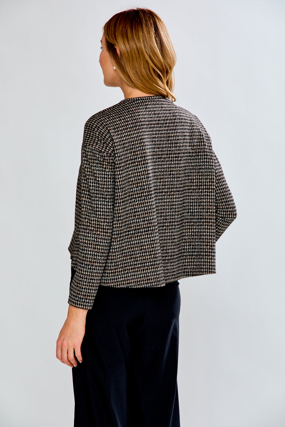 Woman wearing a plaid top with black pants on a light gray background