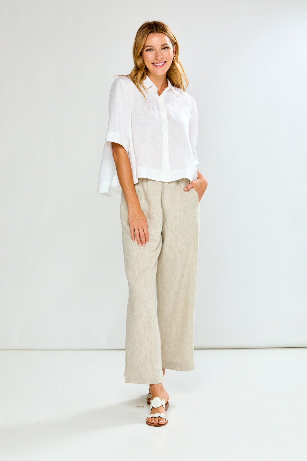 Woman wearing a white blouse and beige pants against a white background