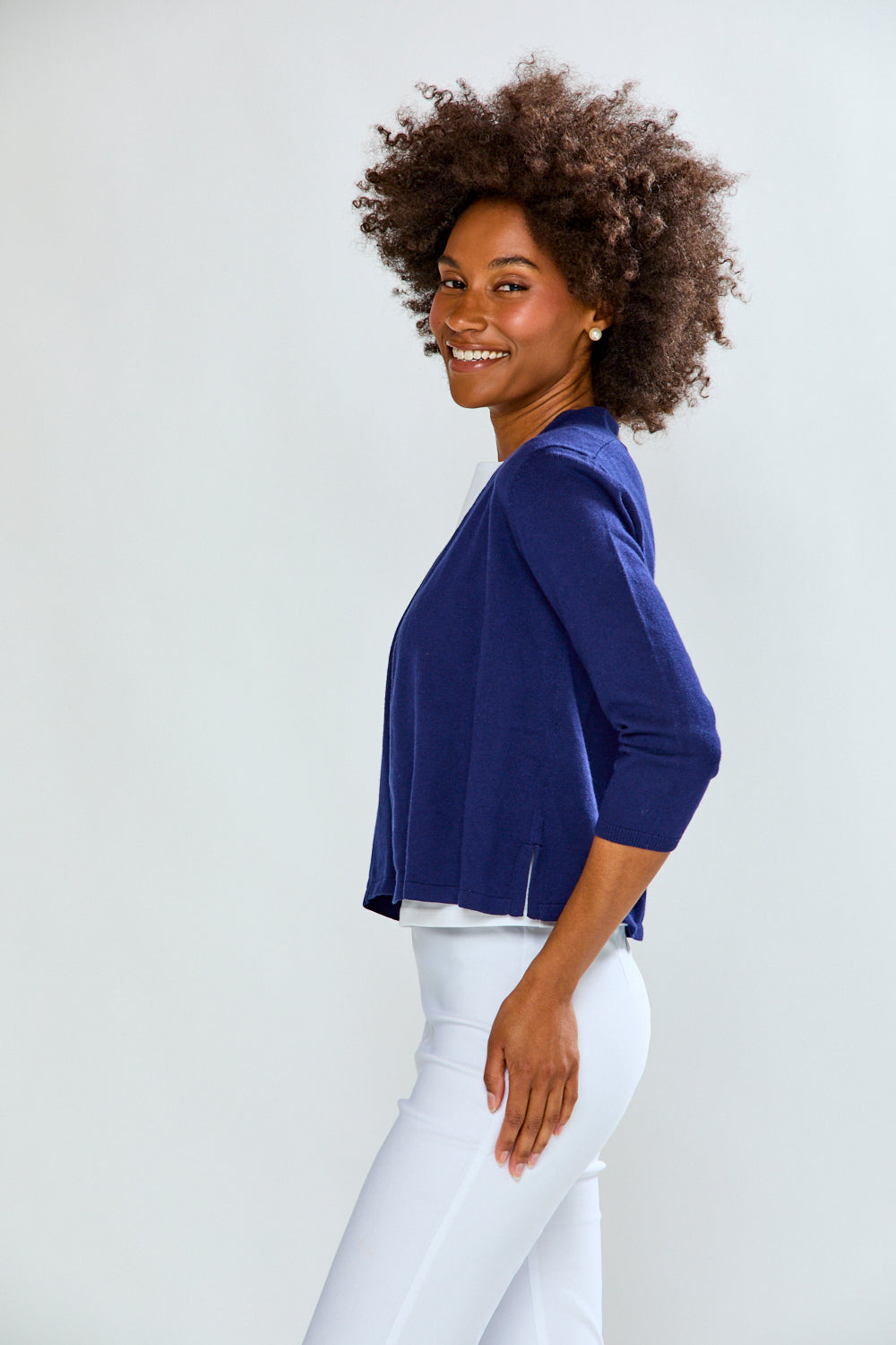 Woman wearing a blue top and white pants against a plain background