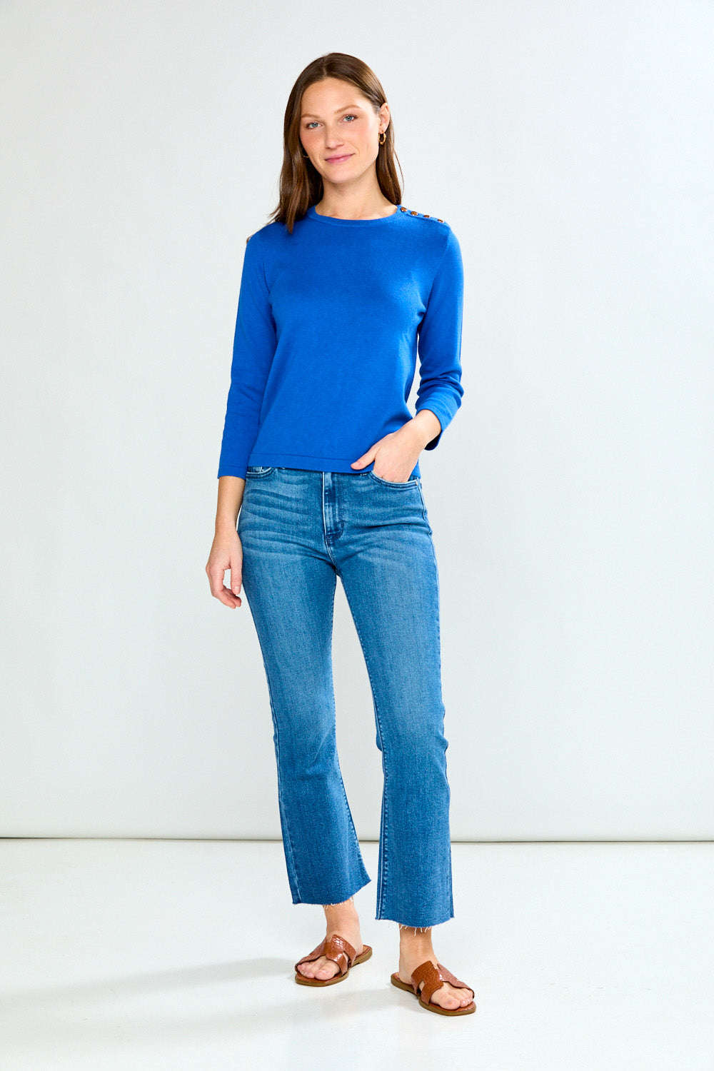 Woman wearing a blue top and jeans against a white background