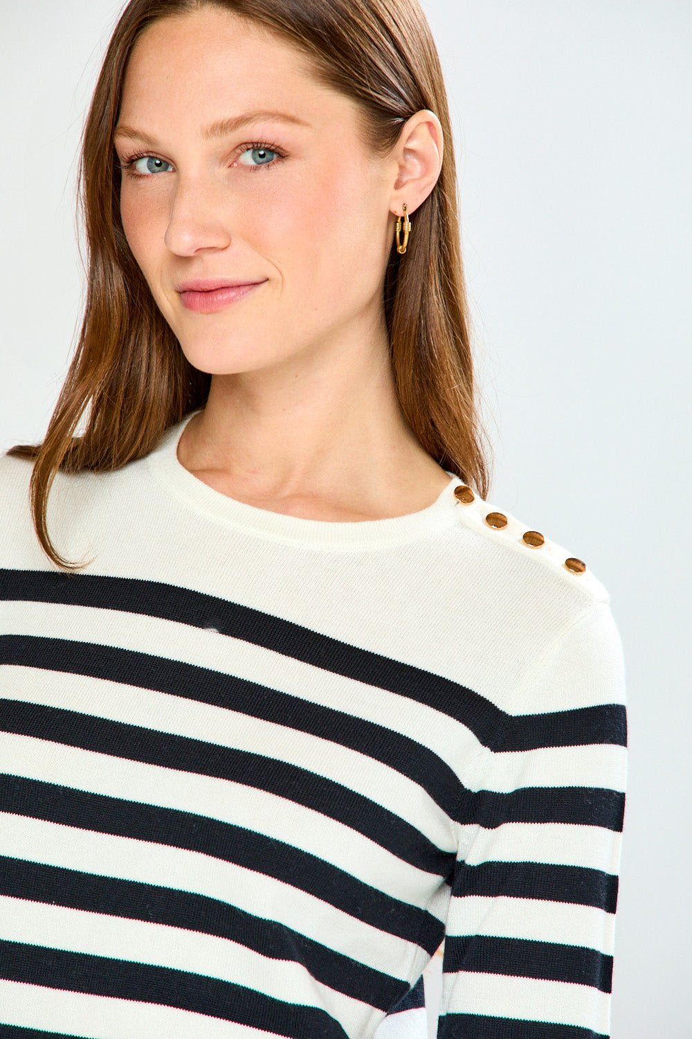Woman wearing a black and white striped sweater with gold buttons on a light gray background