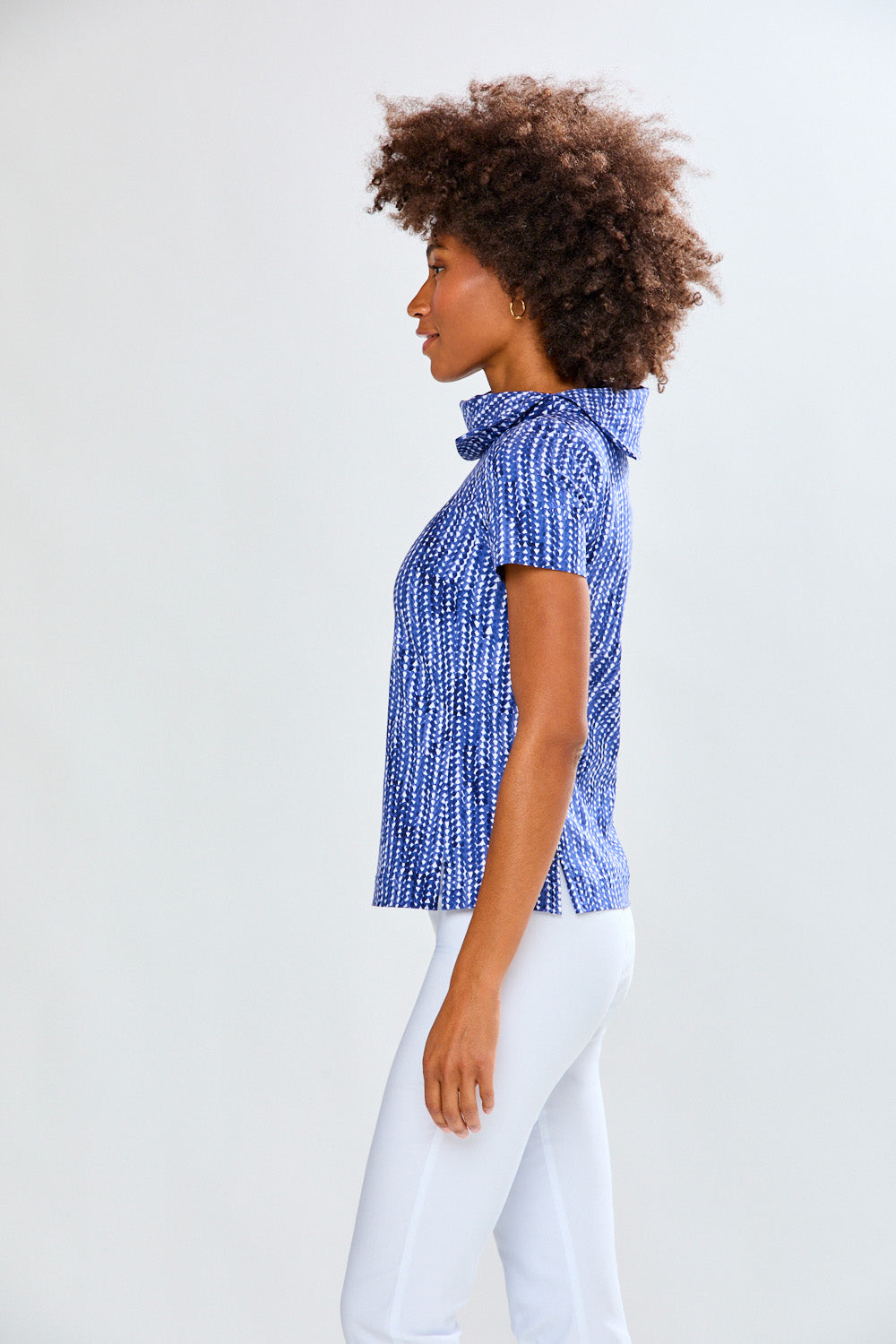Woman wearing a blue patterned top and white pants against a plain background