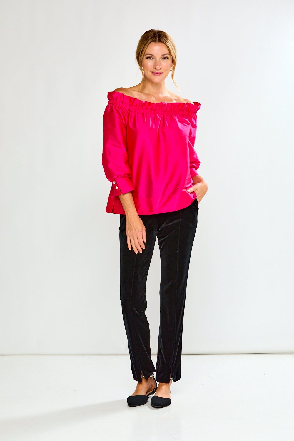 Woman wearing a bright pink off-shoulder top against a white background