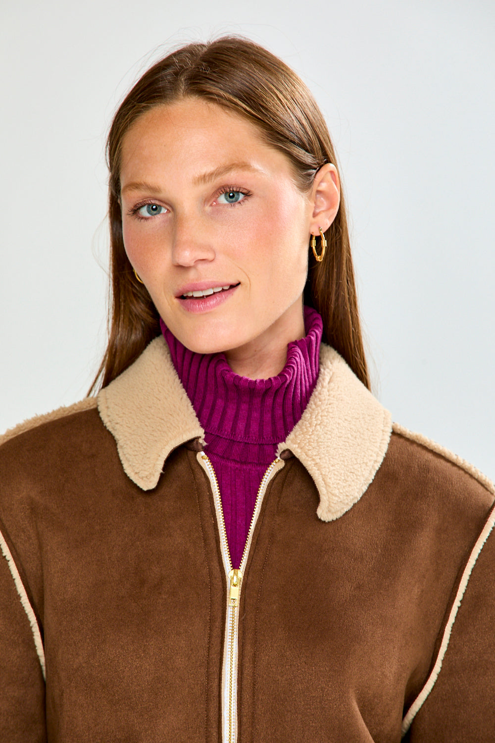 Woman wearing a brown and beige jacket with blue jeans on a white background