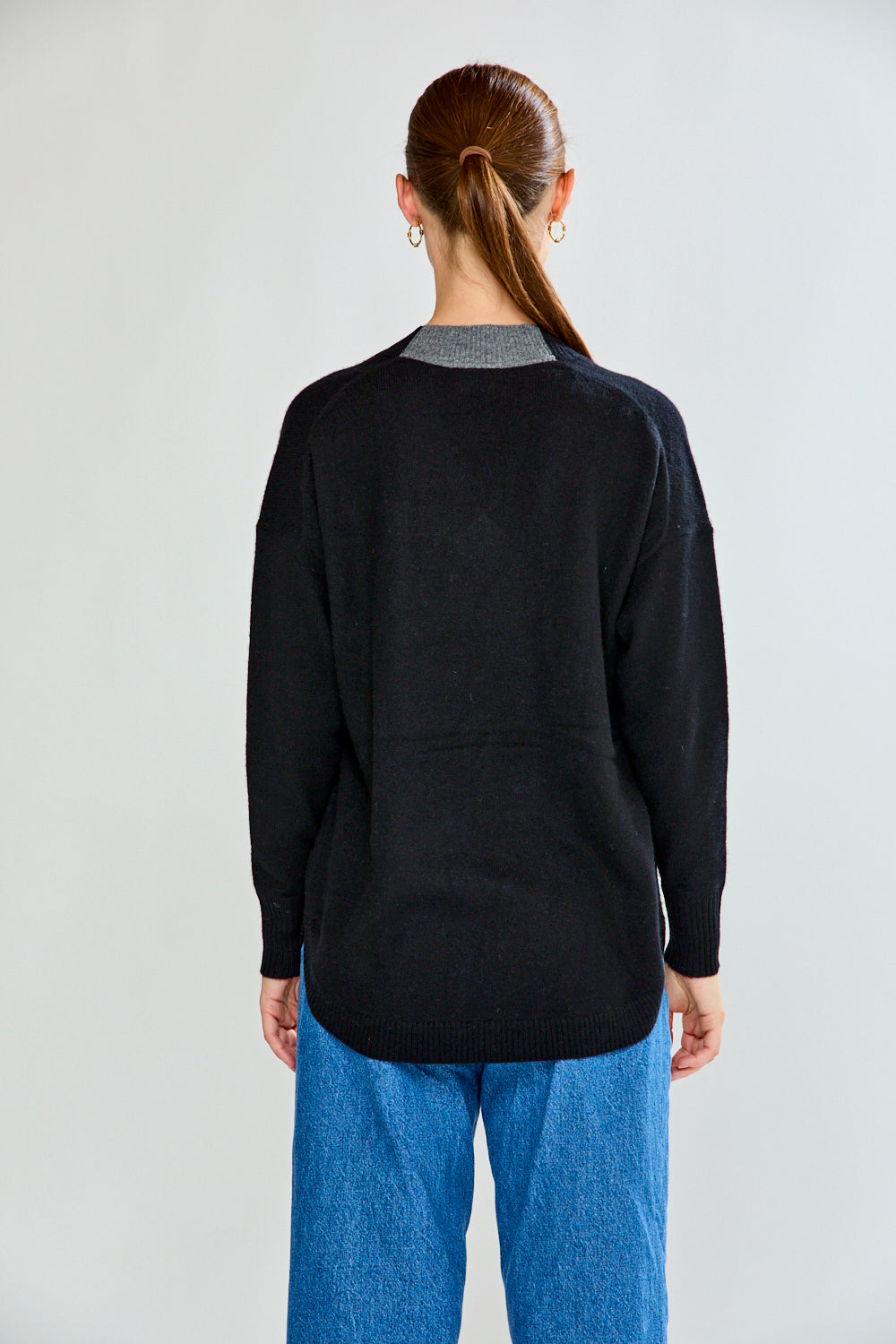 Woman wearing a black sweater and blue jeans against a plain background
