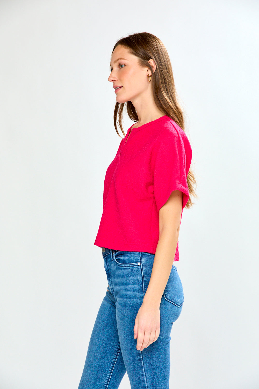 Woman wearing a bright pink top and blue jeans on a white background