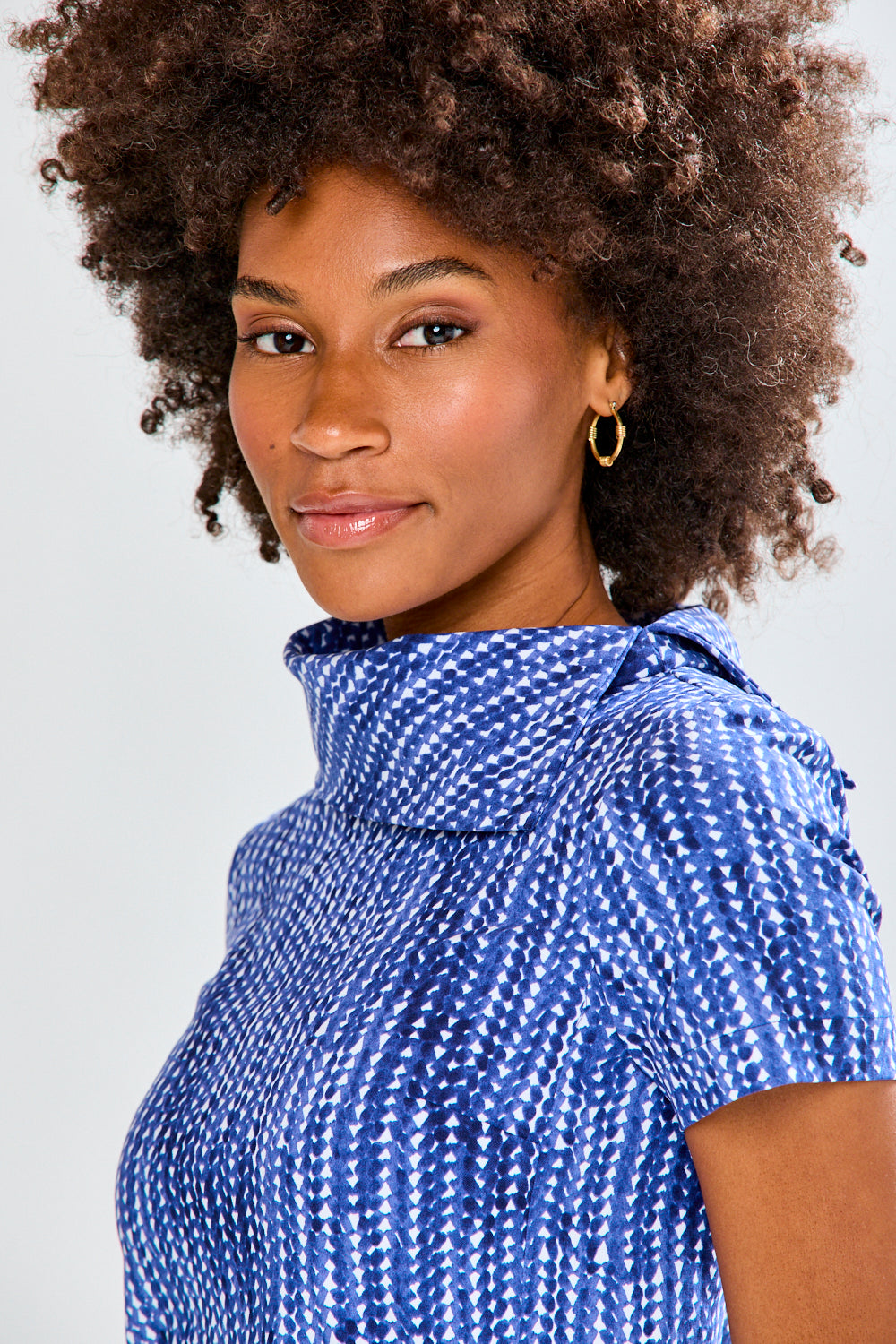Woman wearing a blue patterned top and white pants against a plain background