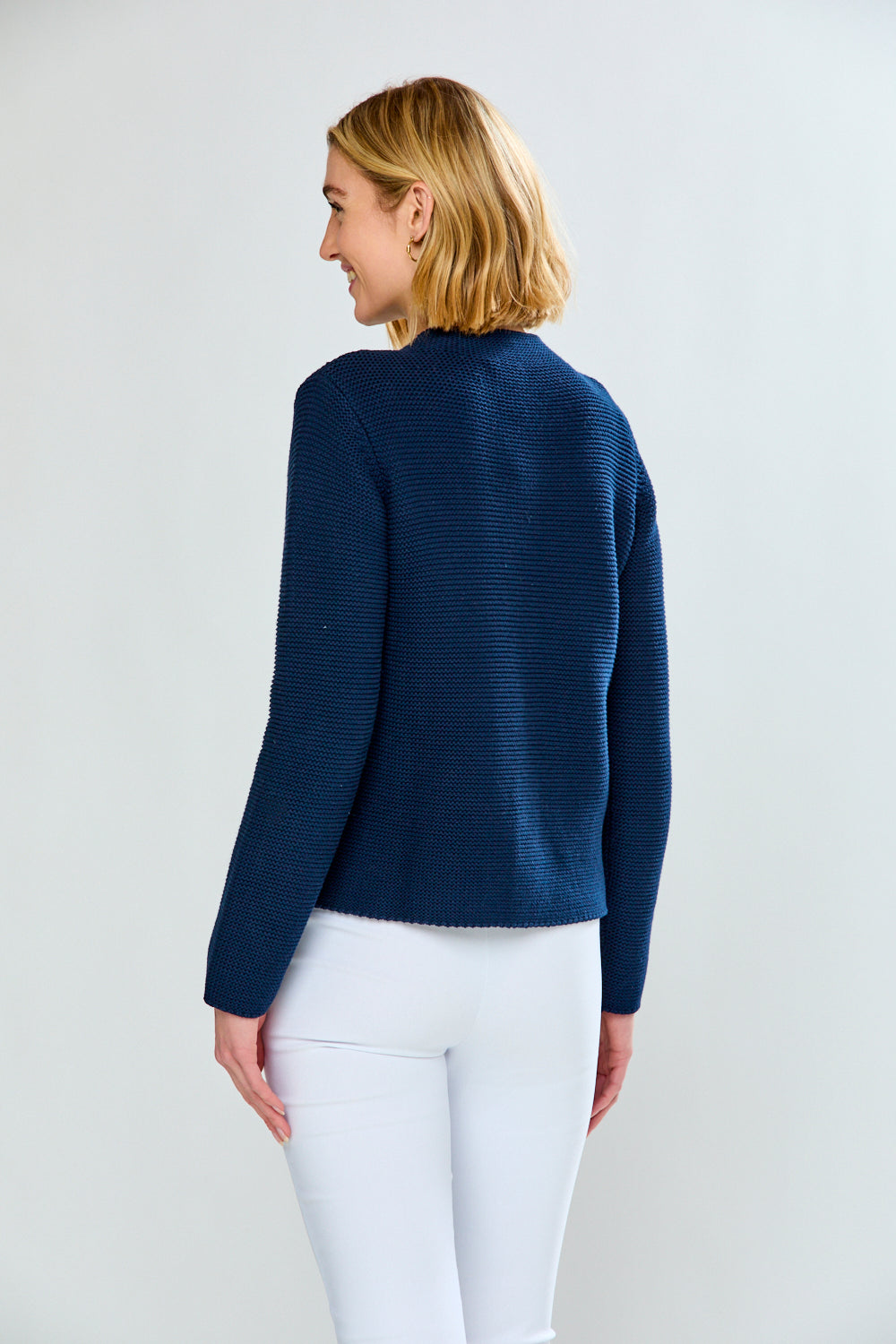 Woman wearing a blue sweater and white pants on a plain background