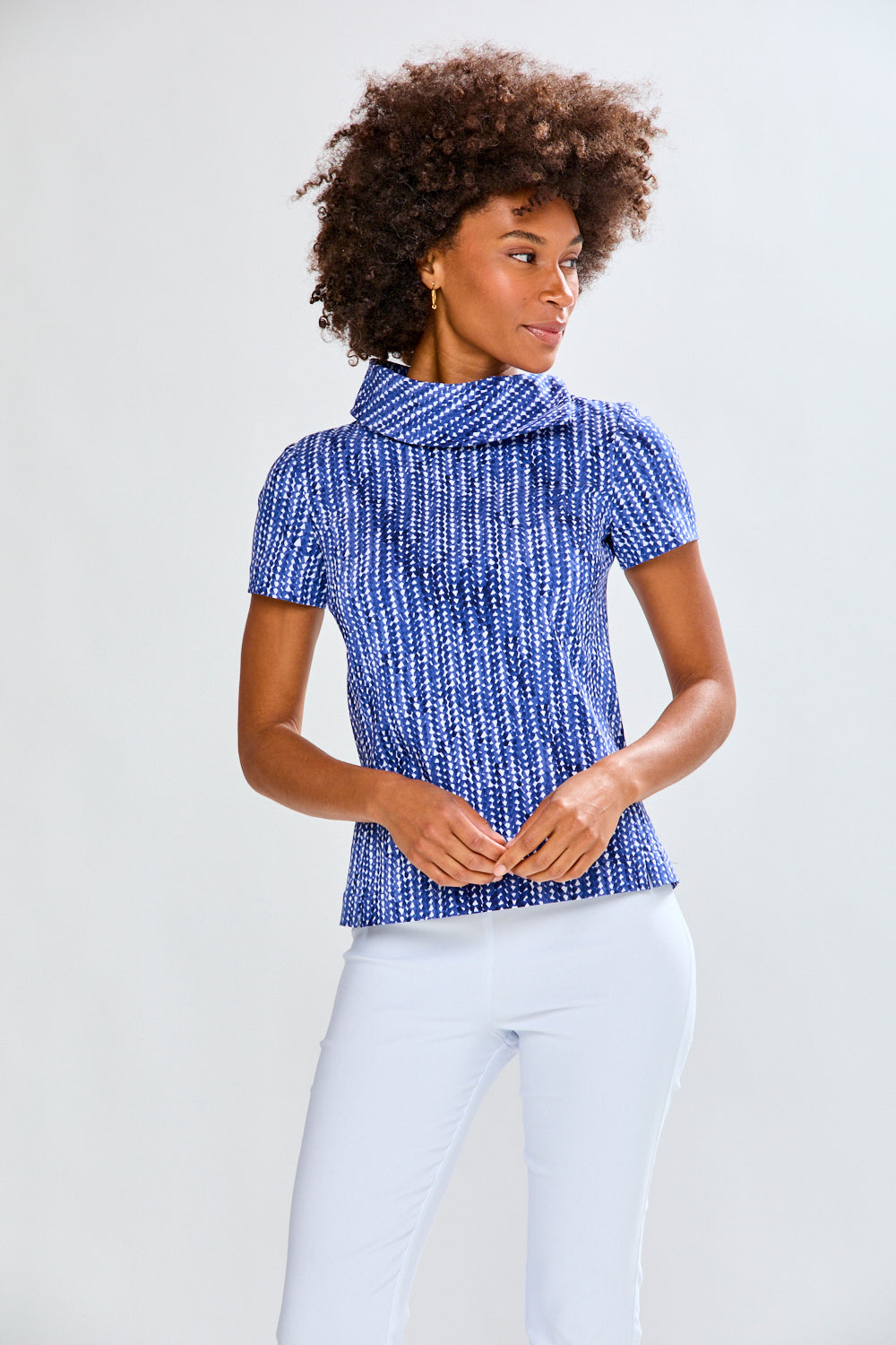 Woman wearing a blue patterned top and white pants against a plain background