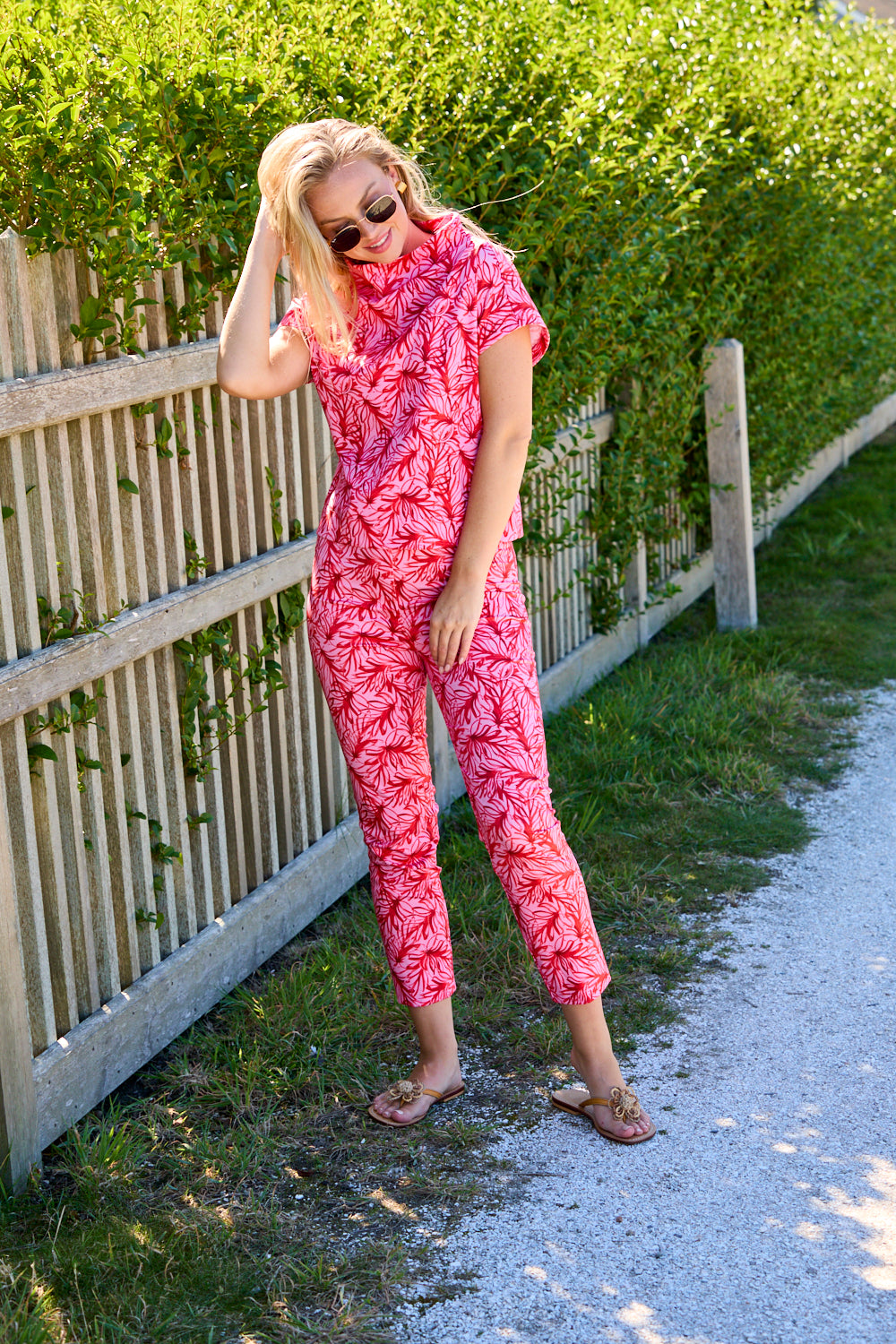 Woman in a pink patterned outfit standing on a path next to a hedge.