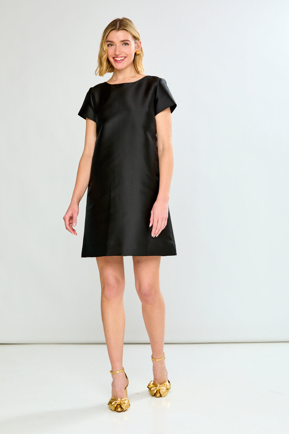 Woman wearing a black dress with gold shoes on a white background