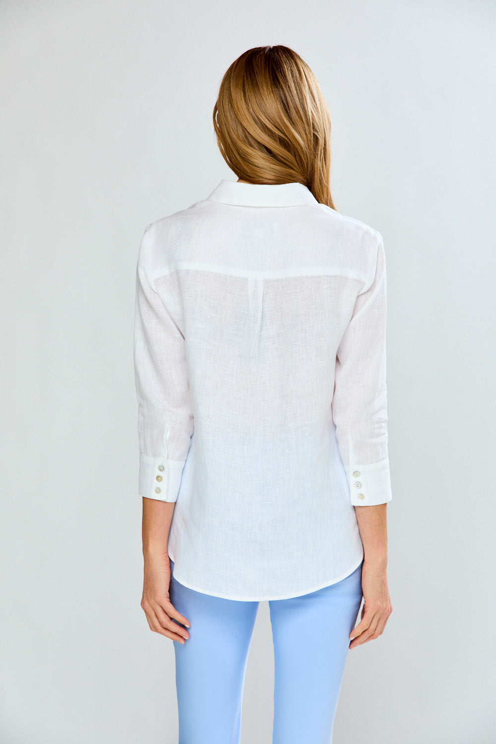 Woman wearing a white blouse with a subtle pattern on a light gray background