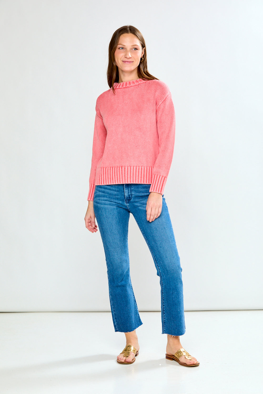 Woman wearing a guava sweater and blue jeans on a white background