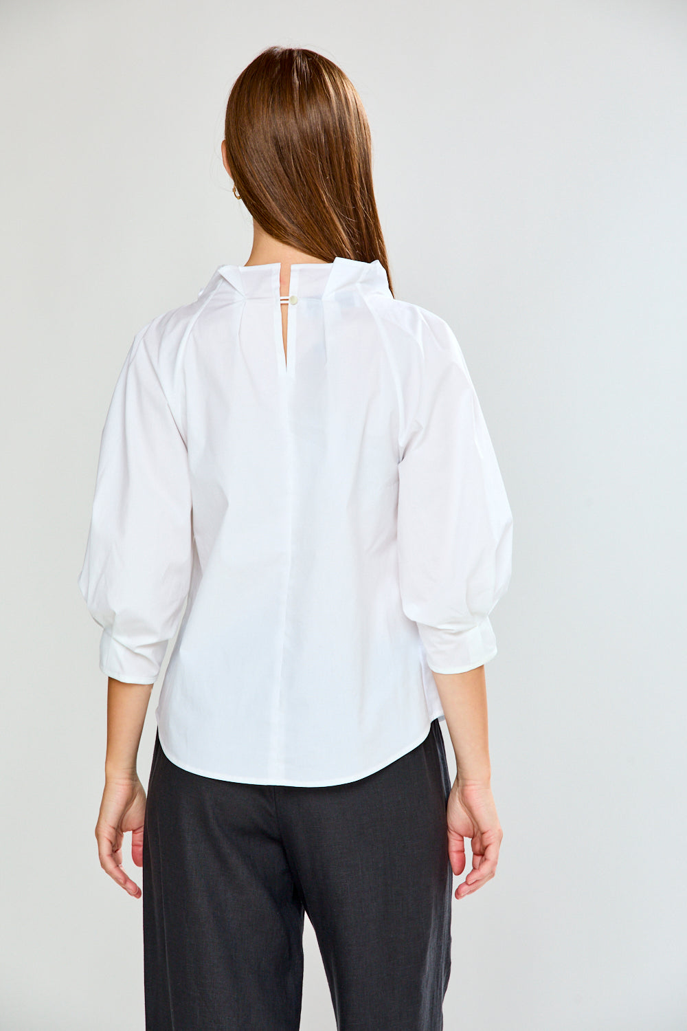 Person wearing a white shirt and black pants on a plain background