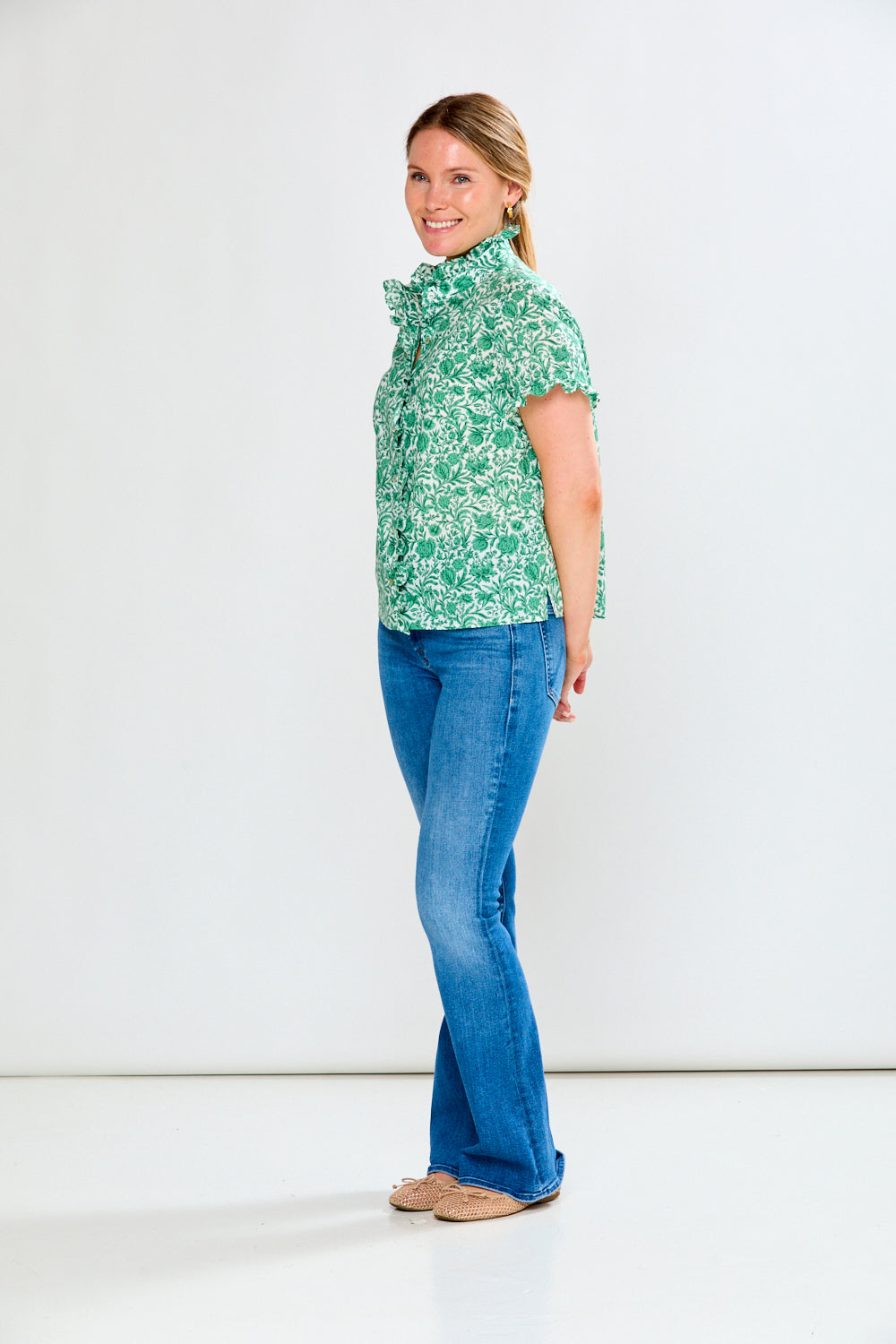 Woman wearing a green patterned blouse and blue jeans on a white background