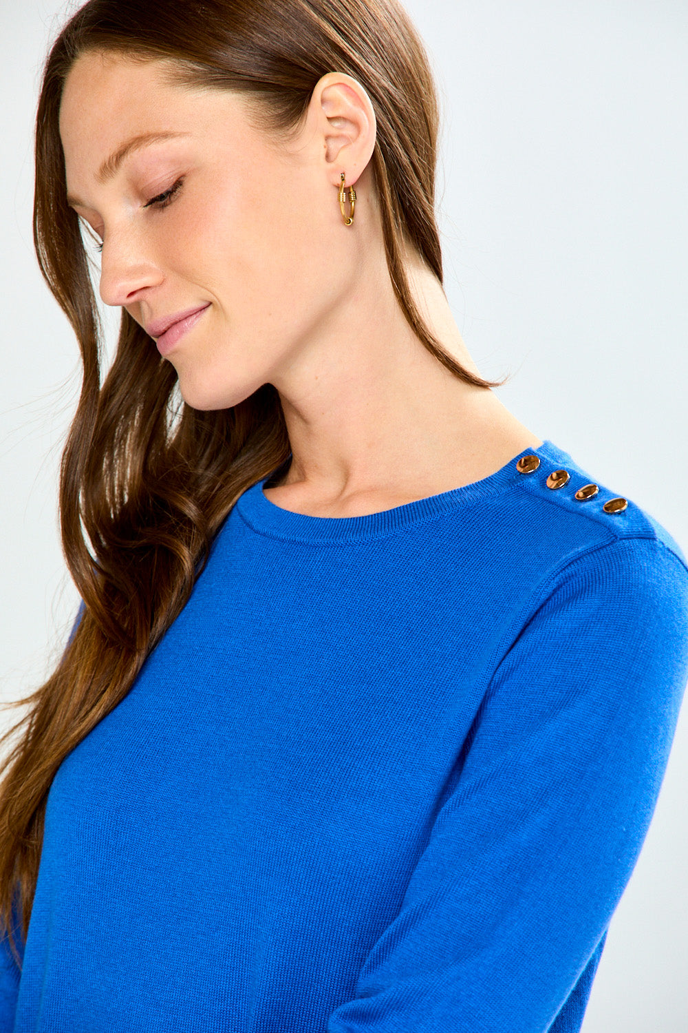 Woman wearing a blue sweater with decorative buttons on a white background