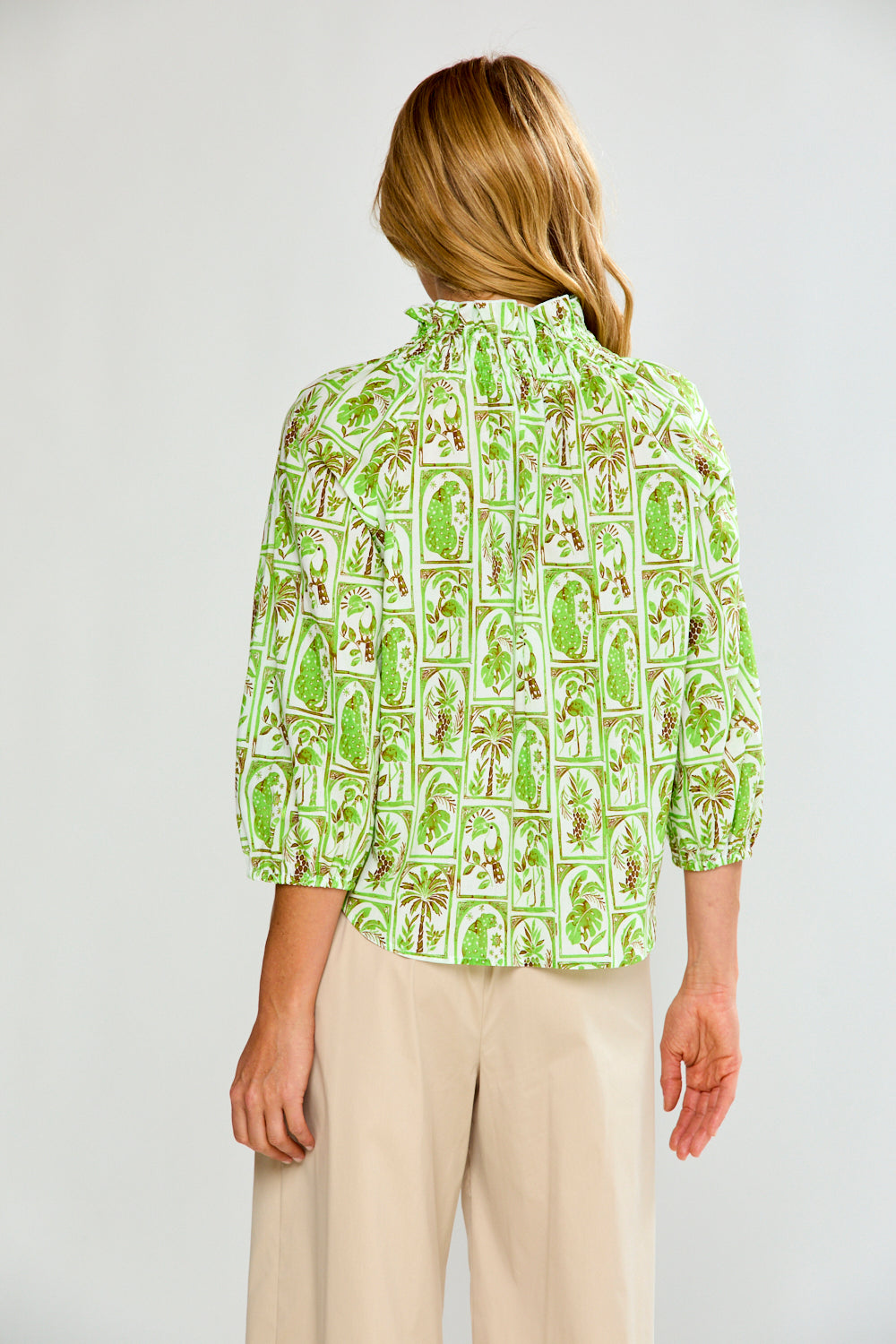 Woman wearing a green patterned blouse and beige pants on a white background