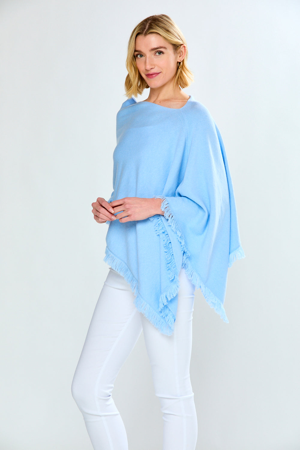 Woman wearing a light blue poncho over a white outfit on a white background