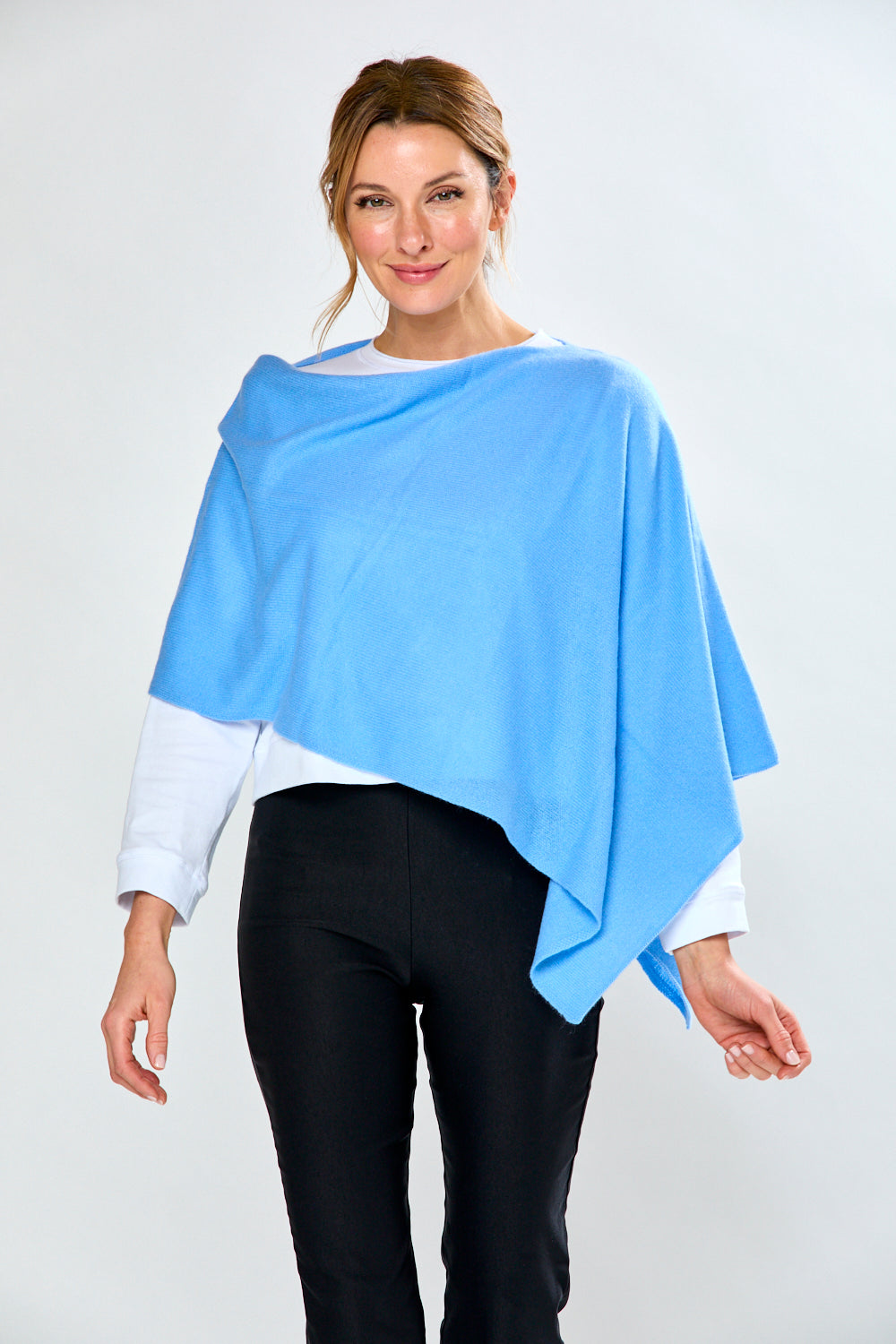 Woman wearing a light blue poncho over a white shirt and black pants on a white background