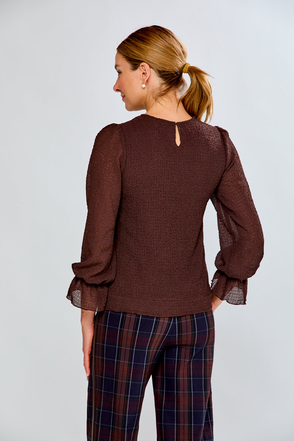 Woman wearing a brown blouse and plaid pants against a light gray background