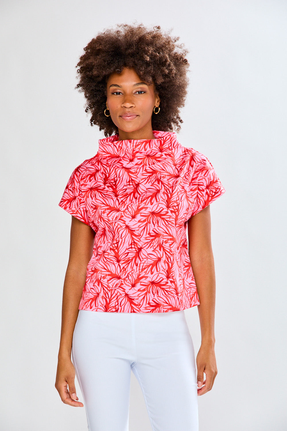 Woman wearing a red patterned top and white pants on a light gray background