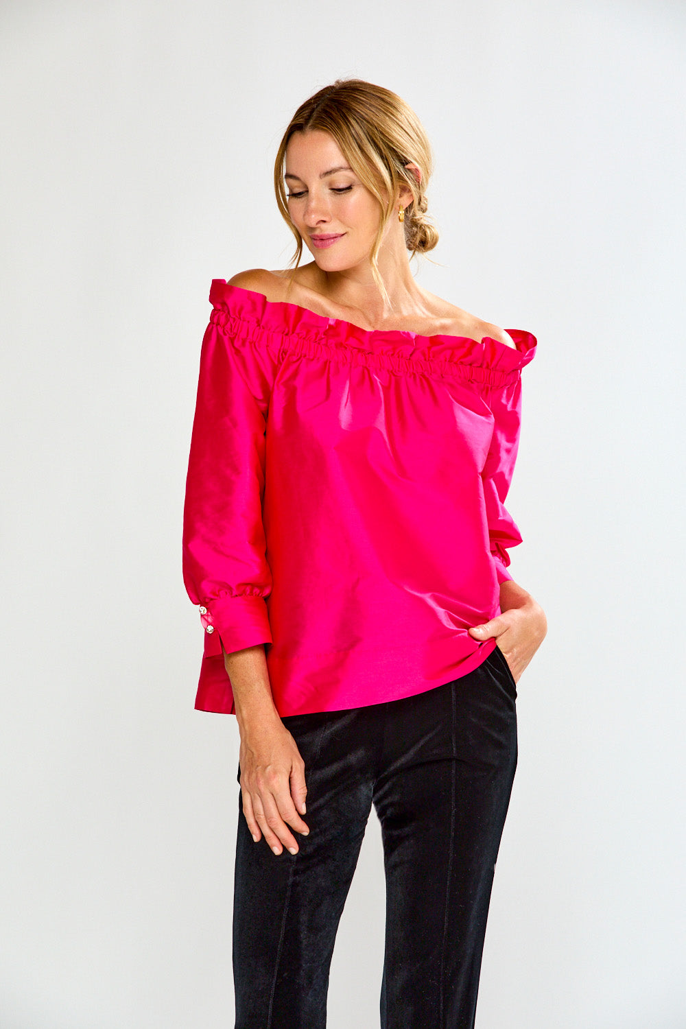 Woman wearing a bright pink off-shoulder top against a white background